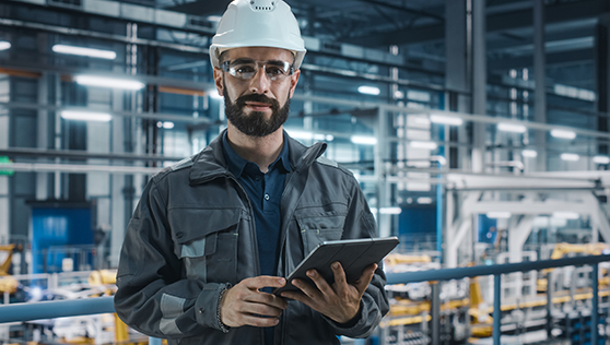 A worker in a hard hat is holding a tablet and giving a demo in a factory.