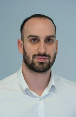 A professional headshot of a man with a beard and a white shirt, set against a plain light blue background, scheduled for corporate use.