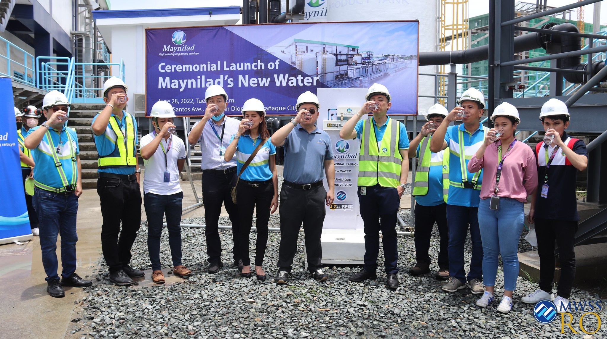 A group of people in safety gear stand outdoors, raising glasses of water to their mouths at the ceremonial launch of Maynilad’s new water treatment facility.