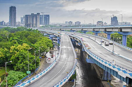 A multi-level flyover with light traffic, surrounded by greenery and high-rise buildings under a cloudy sky—featured in this MicroGenesis Partner Spotlight.