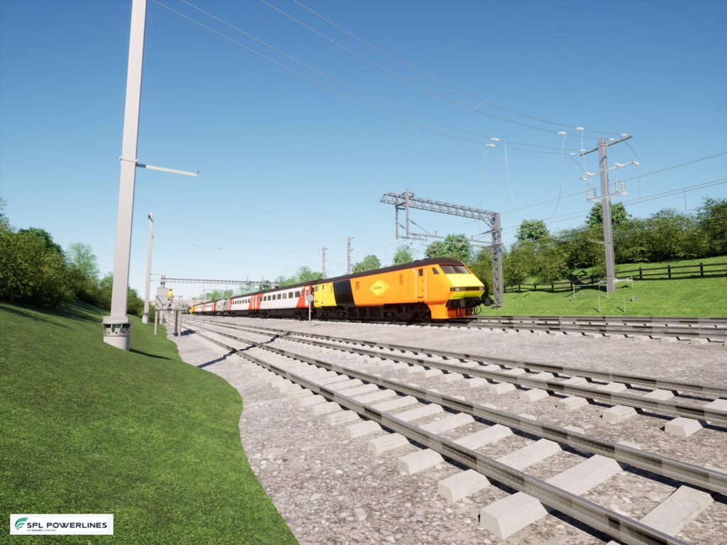 A yellow and orange train travels along railway tracks under overhead electric lines, with green grass and trees on either side.