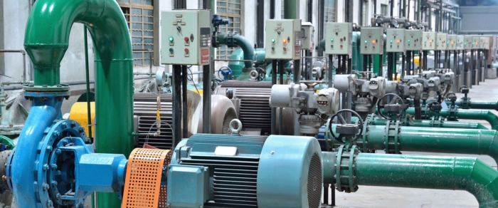 Rząd pomp przemysłowych z silnikami elektrycznymi, podłączonych do zielonych rur i paneli sterowania, zainstalowanych wewnątrz fabryki, w której narzędzia cyfrowe Bentley wspierają wydajną pracę i monitorowanie.