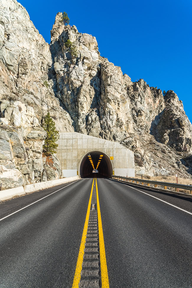 A road leads into a tunnel through the rocky mountains, showcasing an OpenTunnel under the clear blue sky above.