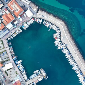 Aerial view of a marina with numerous boats docked along the piers. Nearby buildings line the left side, and clear blue water surrounds the area. Using OpenFlows technology helps manage water flow efficiently, aiming to reduce risk while preserving this coastal gem.