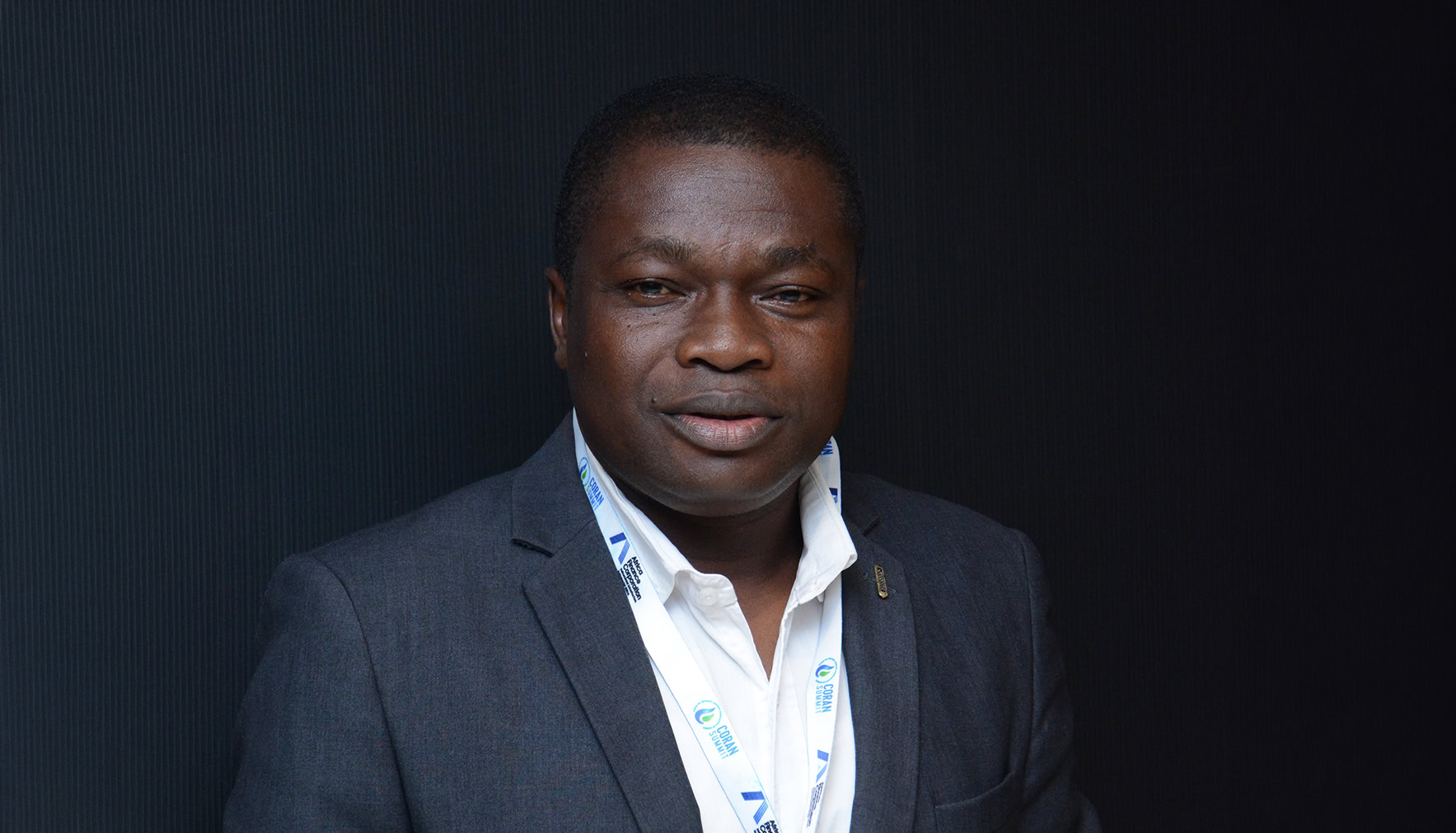 A man in a dark suit and white shirt wearing a lanyard stands in front of a dark background, looking at the camera for this Partner Spotlight.