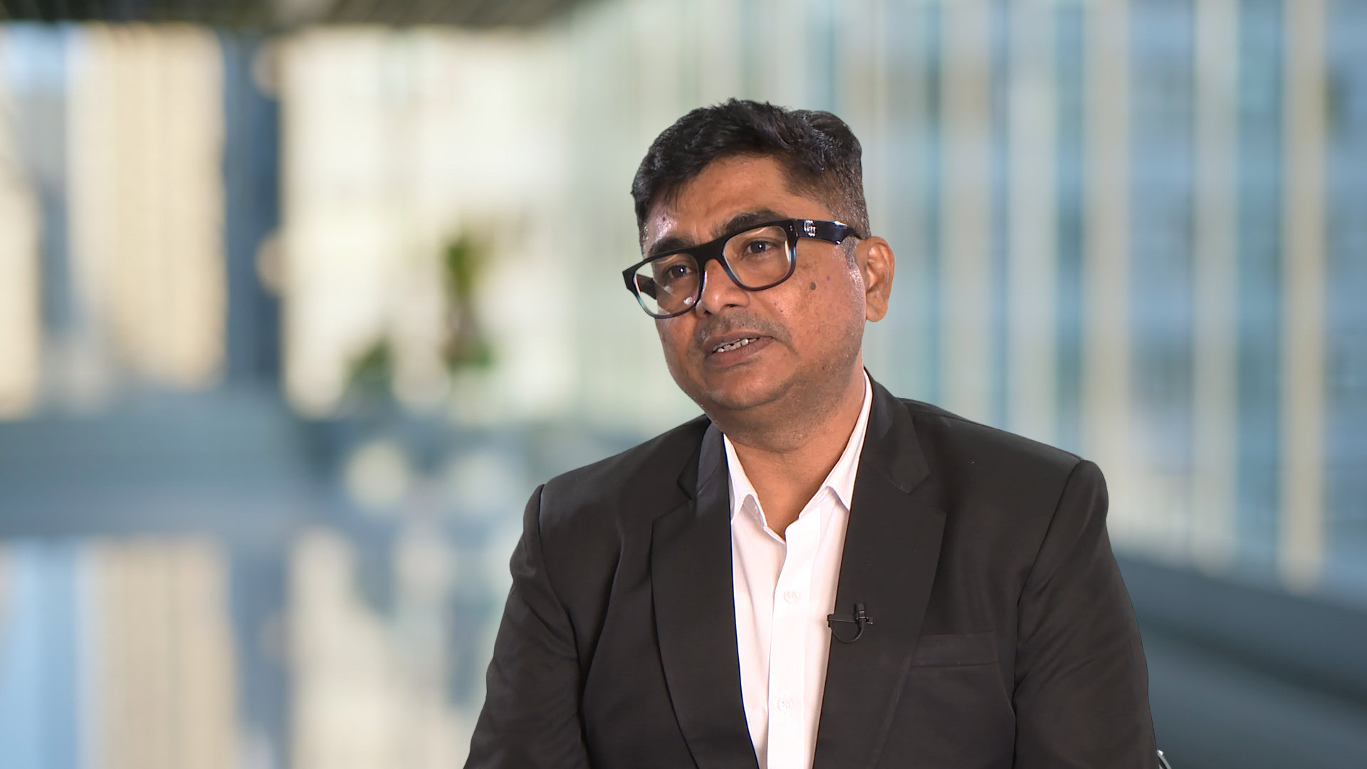 In a light-filled office, a man in glasses and a dark suit sits thoughtfully, embodying the essence of Mahavir Traders in this Partner Spotlight.