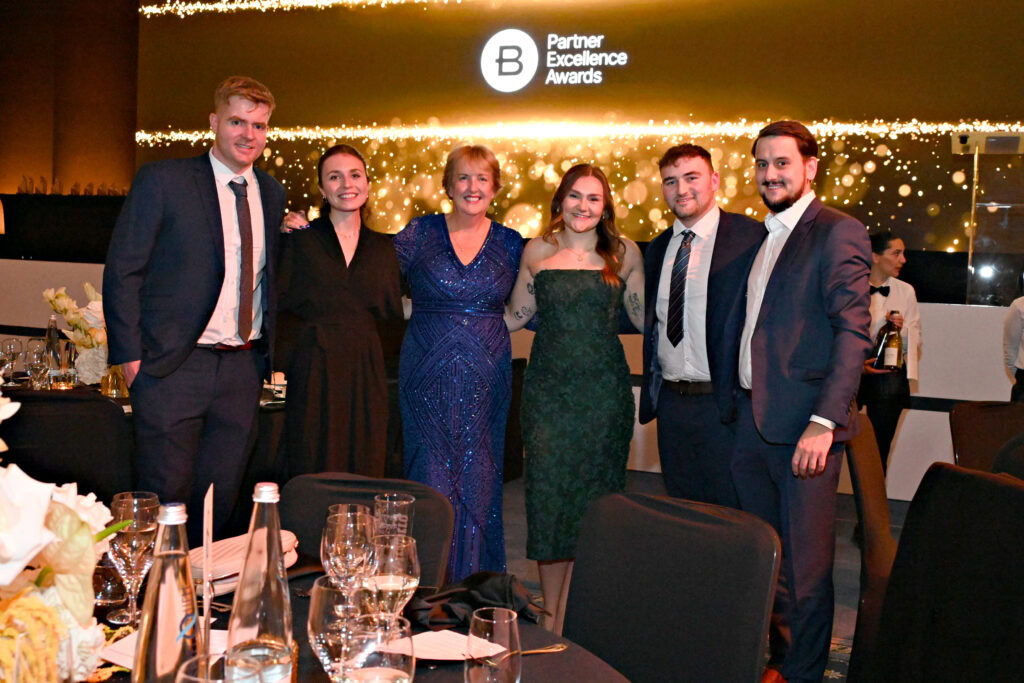 SSix people in formal attire pose together at a round table during the Partner Excellence Awards event.