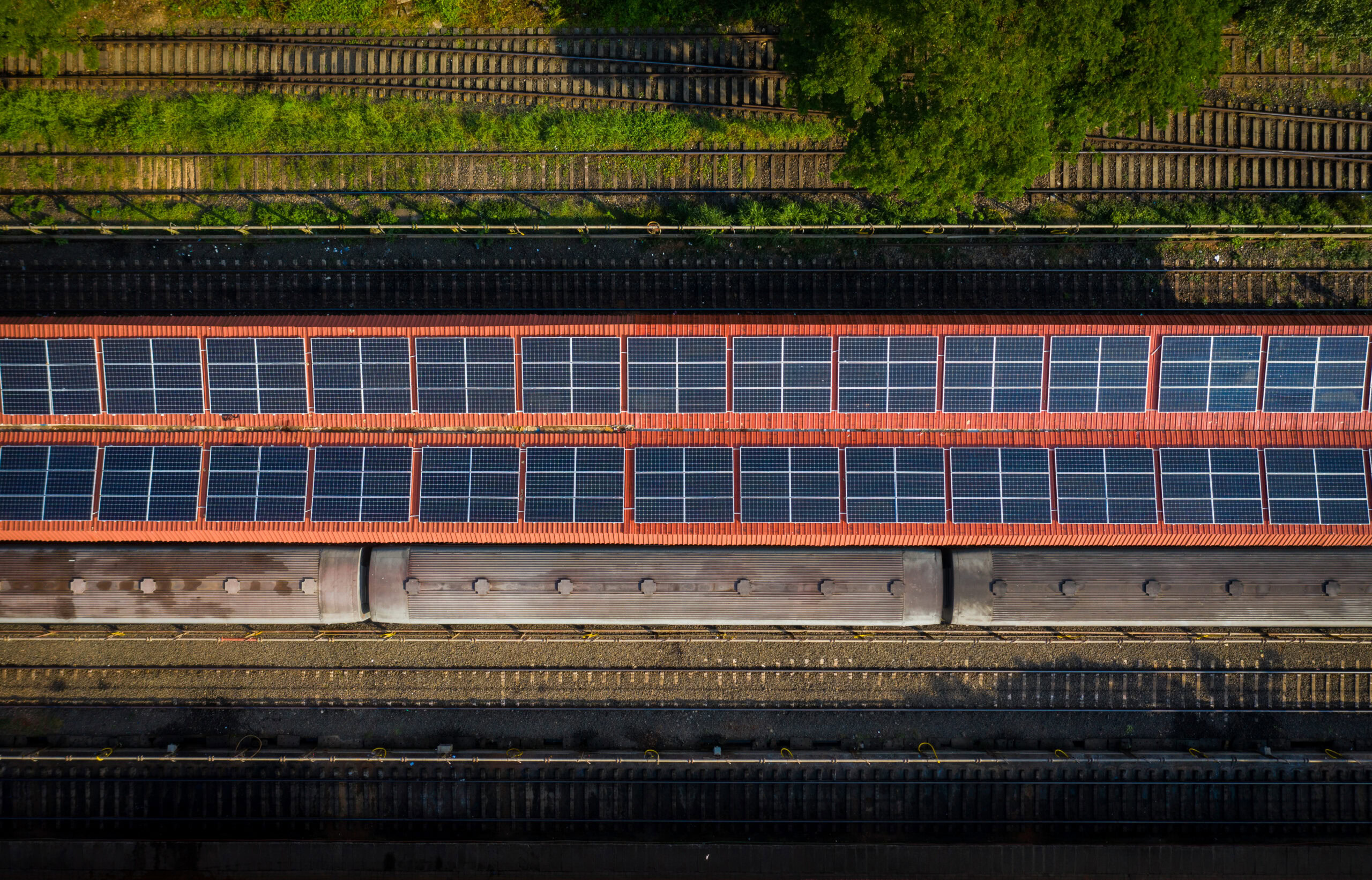 Aerial view of award-winning solar panels installed on the station roof, with a train stopped at the platform, surrounded by railway tracks and greenery.