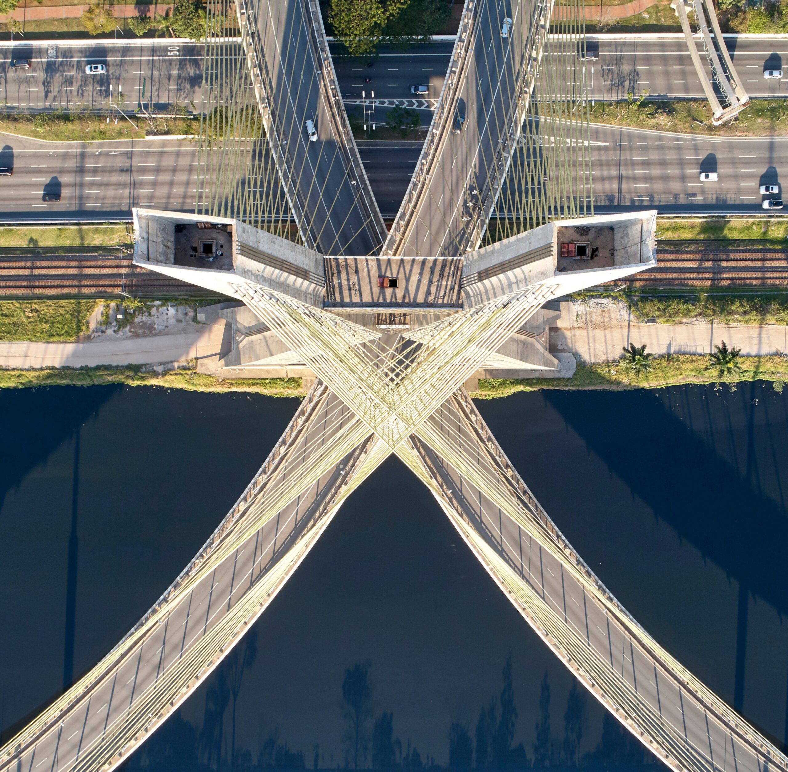 Aerial view of an award-winning cable-stayed bridge with intersecting lanes spanning over a river, featuring cars on surrounding roads and lush green areas on both riverbanks.