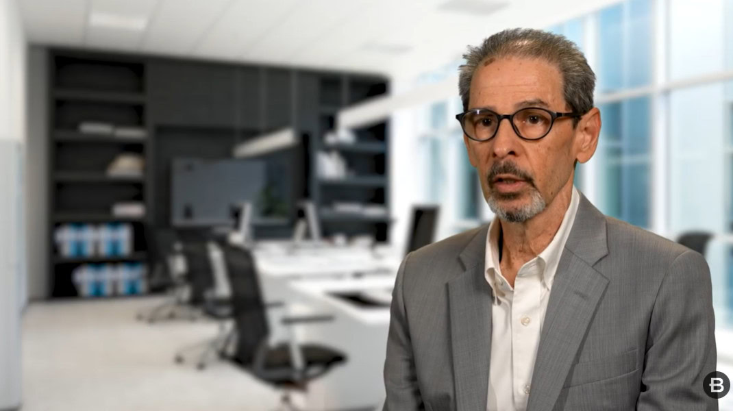 A man in a gray suit and glasses sits in front of a modern office space with desks, chairs, and shelves visible in the background, featured as part of our Partner Spotlight with Astasoft.