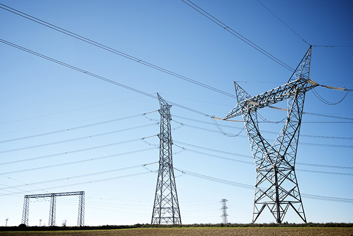 Electrical transmission towers and power lines, designed with advanced Power Line Systems tools like PLS-CADD, stretch across an open landscape under a clear blue sky.