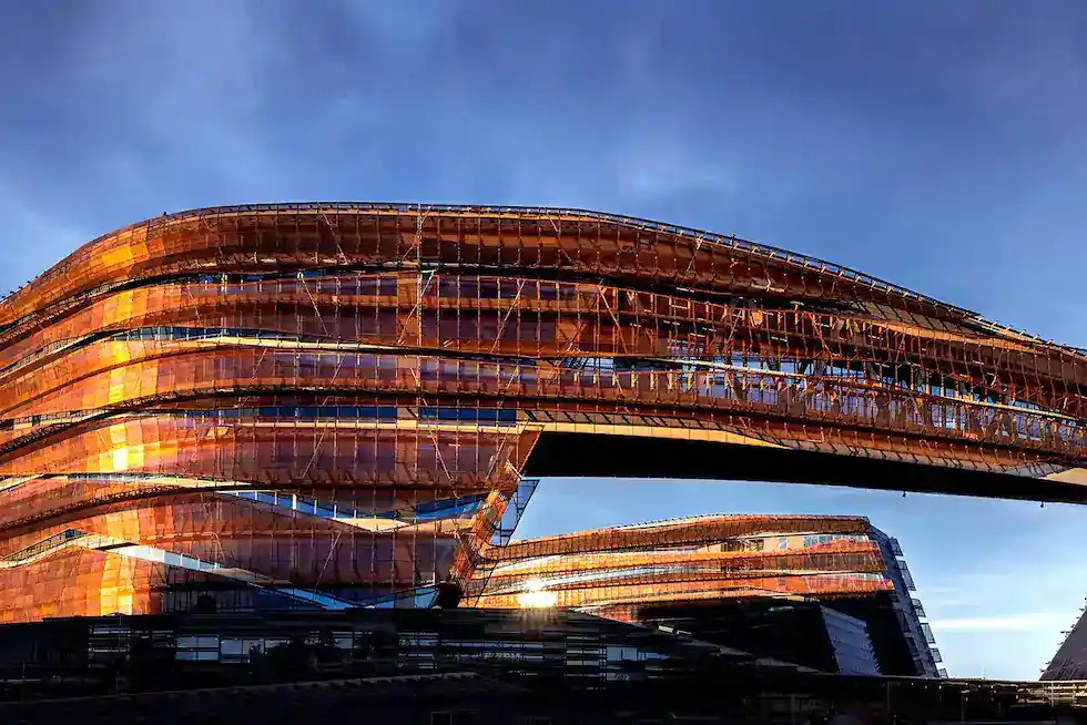 A modern building with angular, layered architecture and a reflective bronze facade under a blue sky.