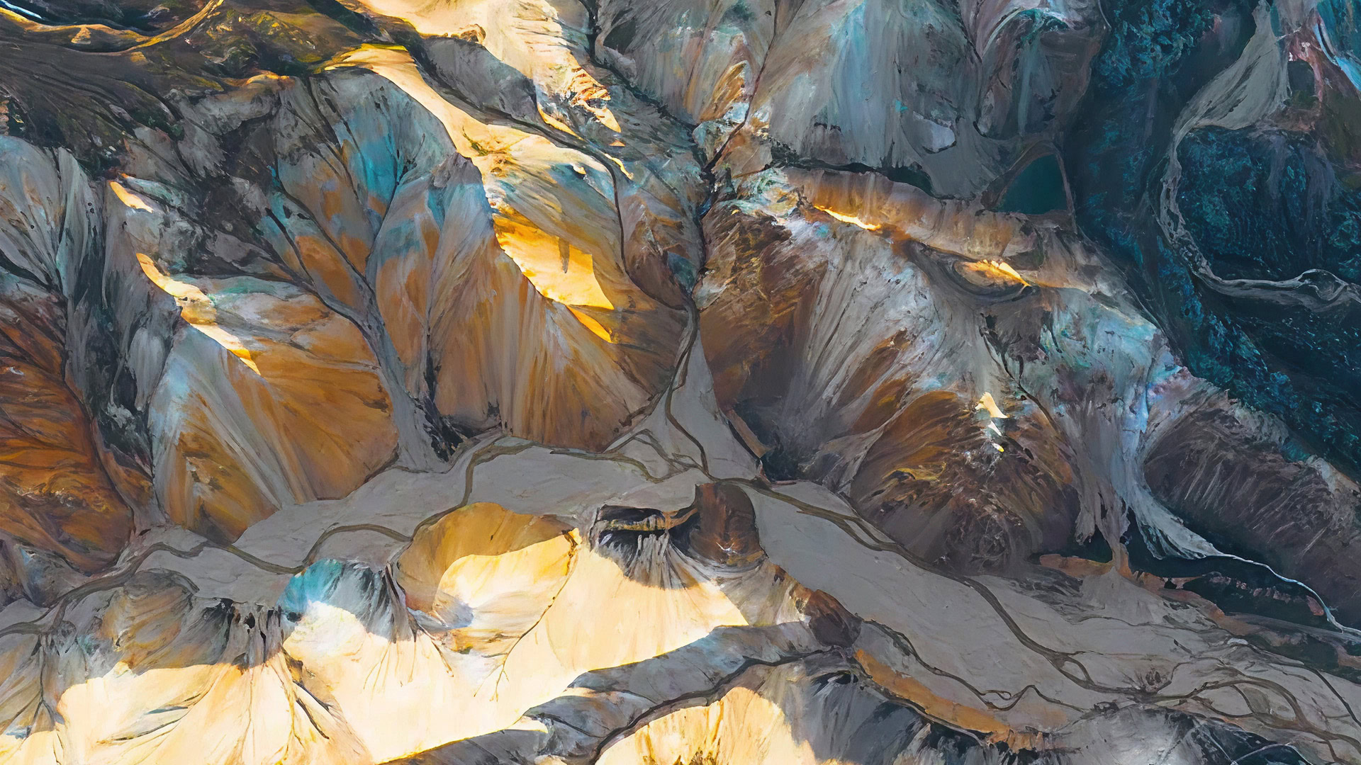 Aerial view of multicolored mountains with yellow, orange, and brown hues, intersected by light-colored valleys and ridges.