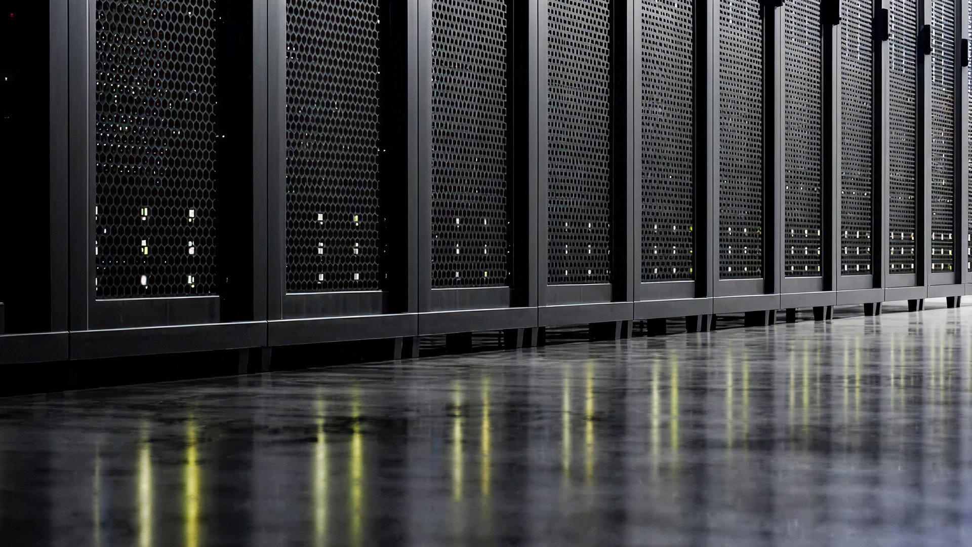 Rows of black server racks with green indicator lights are reflected on a polished floor in a data center.