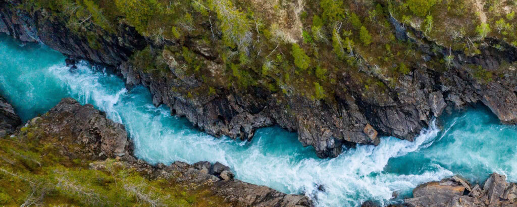 Aerial view of a turquoise river with whitewater rapids flowing through a rocky canyon surrounded by green vegetation, illustrating the efficiency of Sistemas de Distribuição de Água in maintaining such natural beauty.