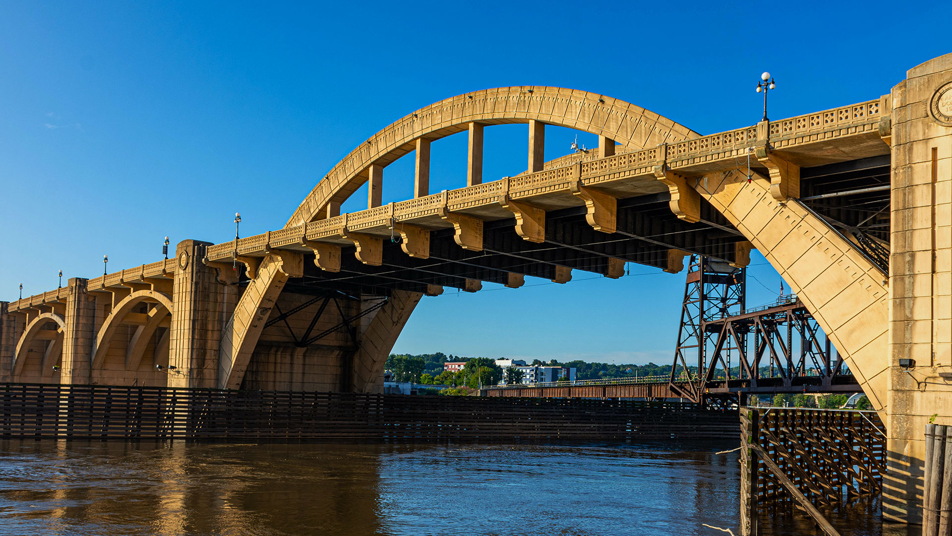 A large concrete arch bridge, pivotal for transportation services, spans across a river with clear blue skies in the background.