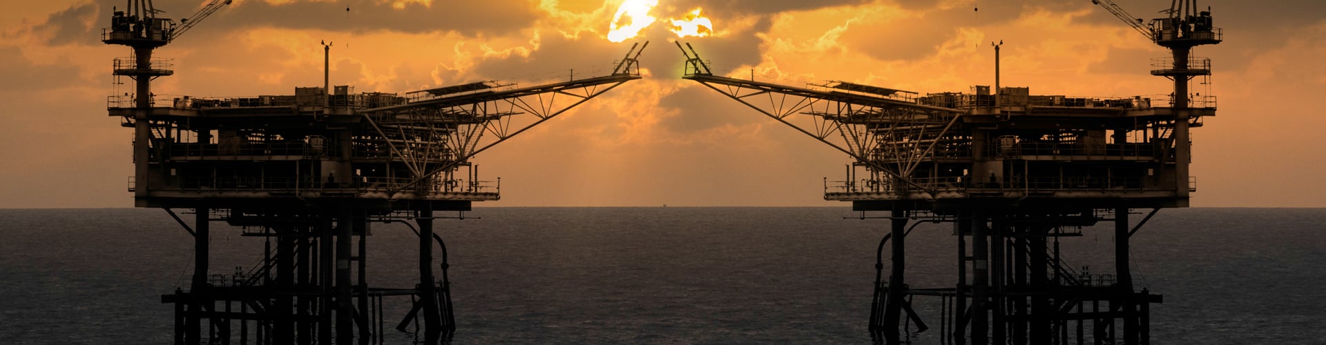 Two offshore oil platforms with flaring gas set against a dramatic sunset over the ocean, showcasing the beauty and complexity of SACS-enabled offshore design.
