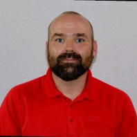 A man with a beard and short hair wearing a bright red polo shirt poses for an ID-style photo, reminiscent of an engineer ready to tackle OpenFlows water management projects.
