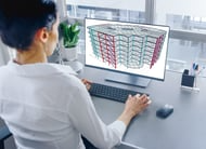 A person at a desk uses a computer to view a 3D model of a multi-story building, leveraging Structural WorkSuite for precise analysis. Nearby, case studies offer insights into similar architectural projects.