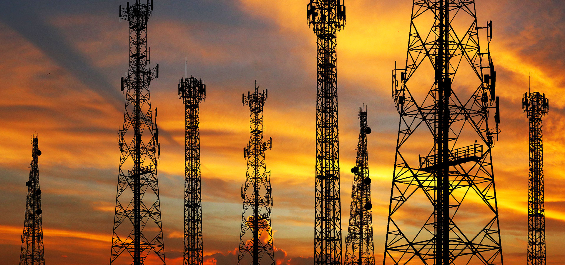 A group of communication towers are silhouetted against a vibrant sunset sky, showcasing their sleek design.
