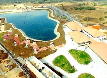 Aerial view of a coastal resort with a kidney-shaped pool, adjacent buildings, and surrounding green areas bordering a natural body of water optimized with SEO keywords.