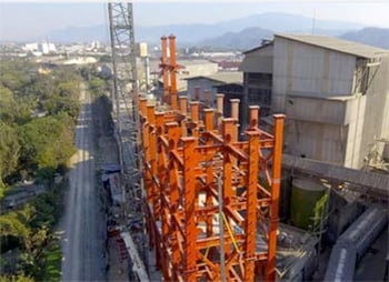 Aerial view of a construction site with orange scaffolding alongside an industrial building, featuring structural worksuite, with a cityscape in the background.