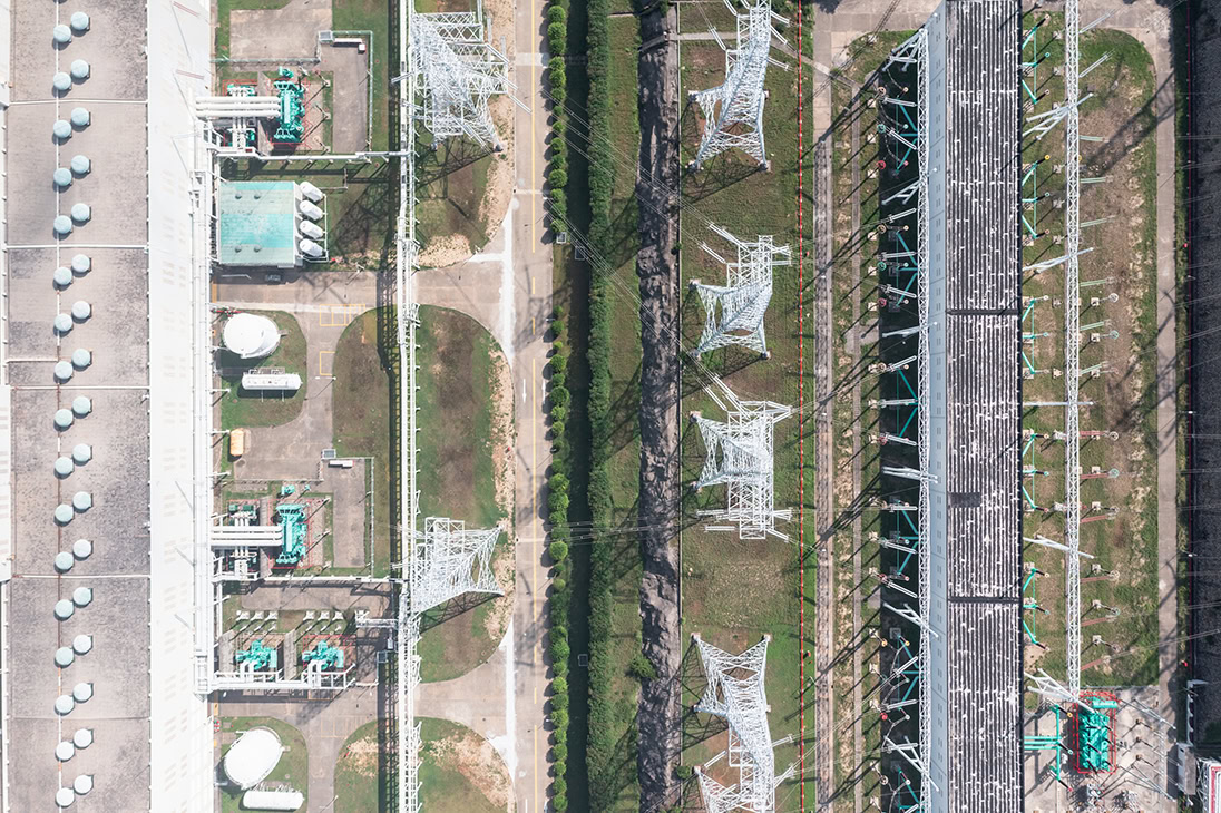 Aerial view of an industrial complex featuring machinery, pipelines, and electric utilities infrastructure, with transmission towers arranged in parallel lines.