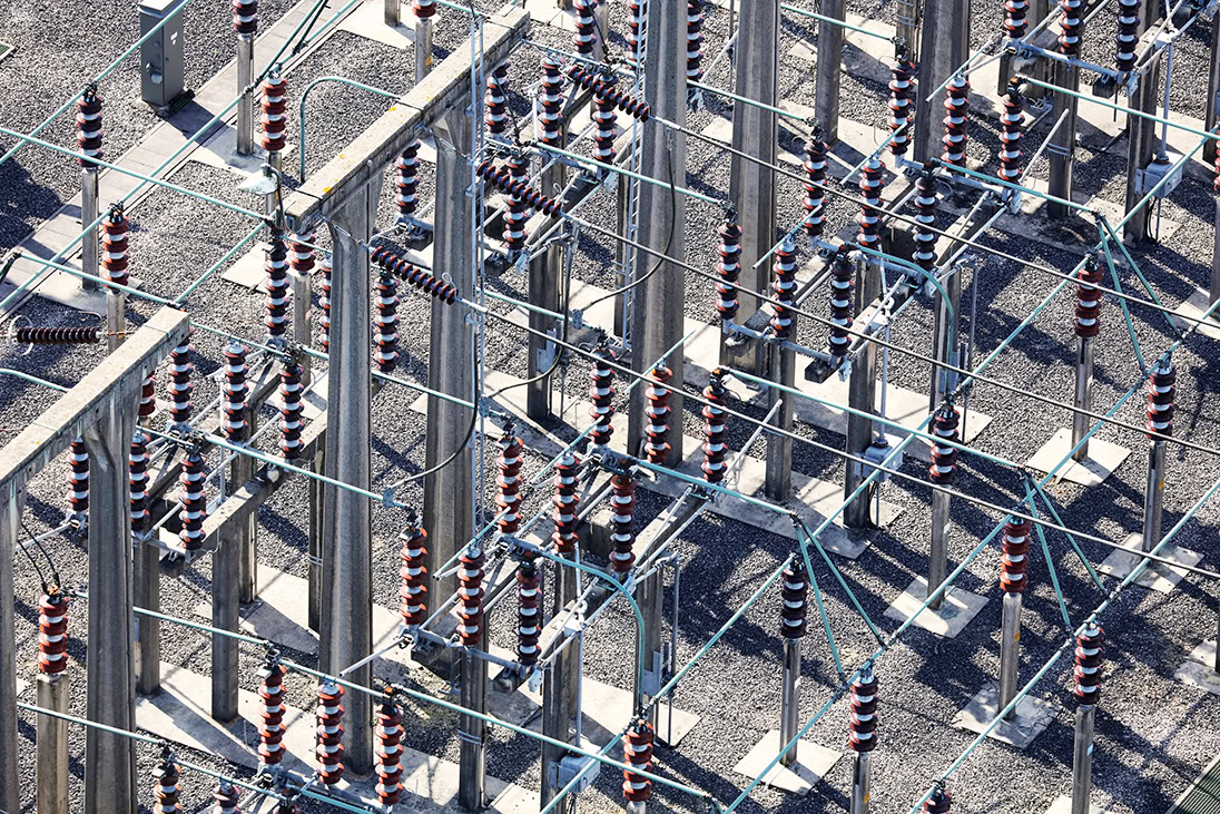 Aerial view of an electrical substation operated by electric utilities, featuring metal structures, insulators, and connecting wires arranged in a grid pattern.