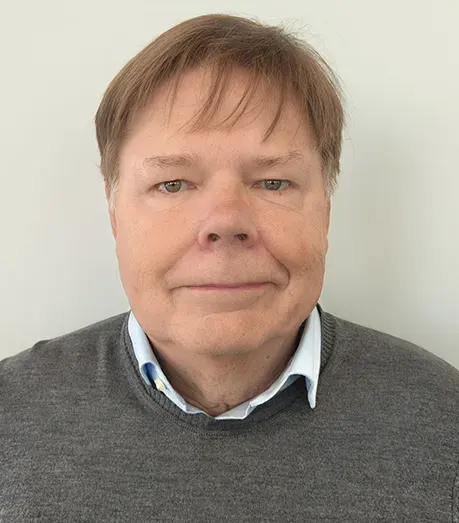 A middle-aged man with light brown hair wearing a grey sweater over a collared shirt