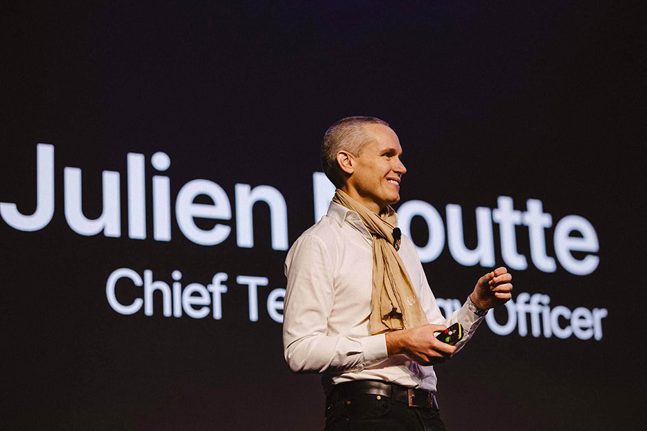 A man stands on stage giving a presentation, with the large text "Julien Moutte, Chief Technology Officer" and a tagline reading "The Man Who Opens Everything" displayed behind him.
