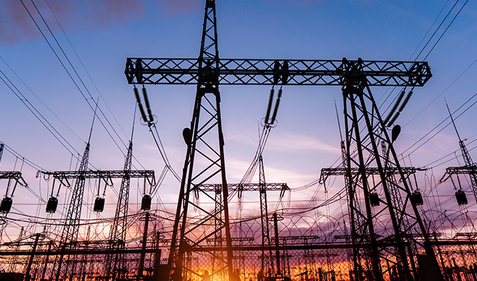 Electrical substation with power lines and towers silhouetted against a sunset sky.