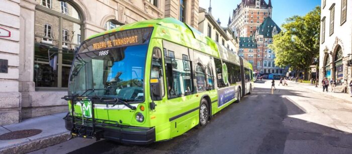 A bright green articulated city bus labeled "Réseau de transport" is parked on a street in a historic urban area with stone buildings and a castle-like structure in the background.
