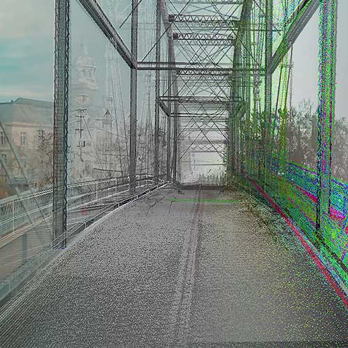 A distorted image of a metal truss bridge with visible digital noise and color glitches, showing buildings and trees in the background.