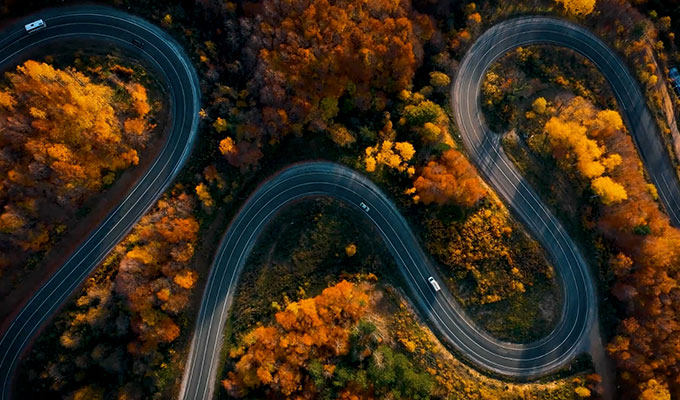 Luftaufnahmen einer kurvigen Straße im Herbst, eines wunderschönen geschwungenen Passes mit Fahrzeugen in einer bunten Herbstlandschaft mit Bäumen bei Sonnenuntergang