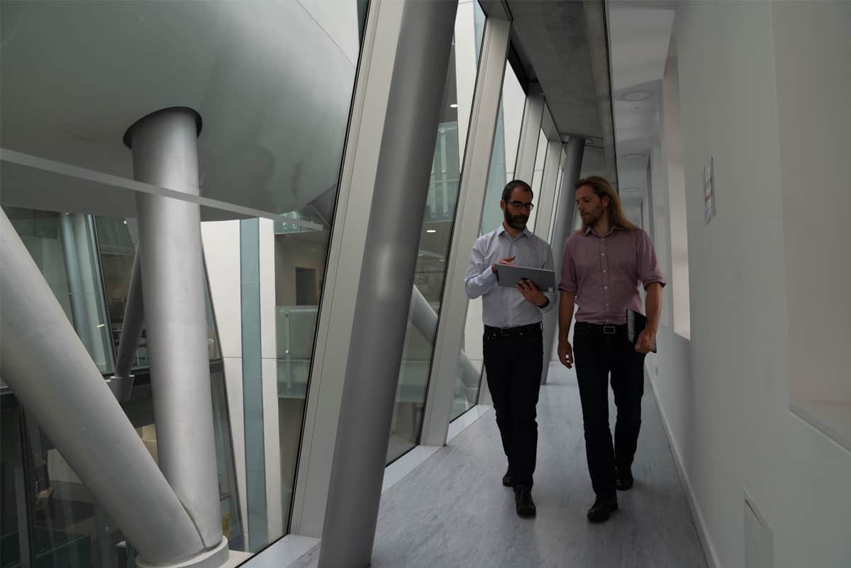 Two men looking at an iPad as they walk down a hallway at an office building