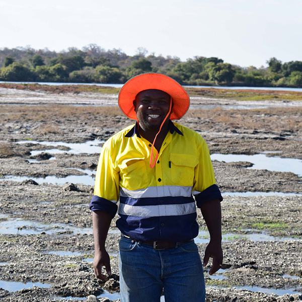 A man in a yellow hat standing in a muddy area.