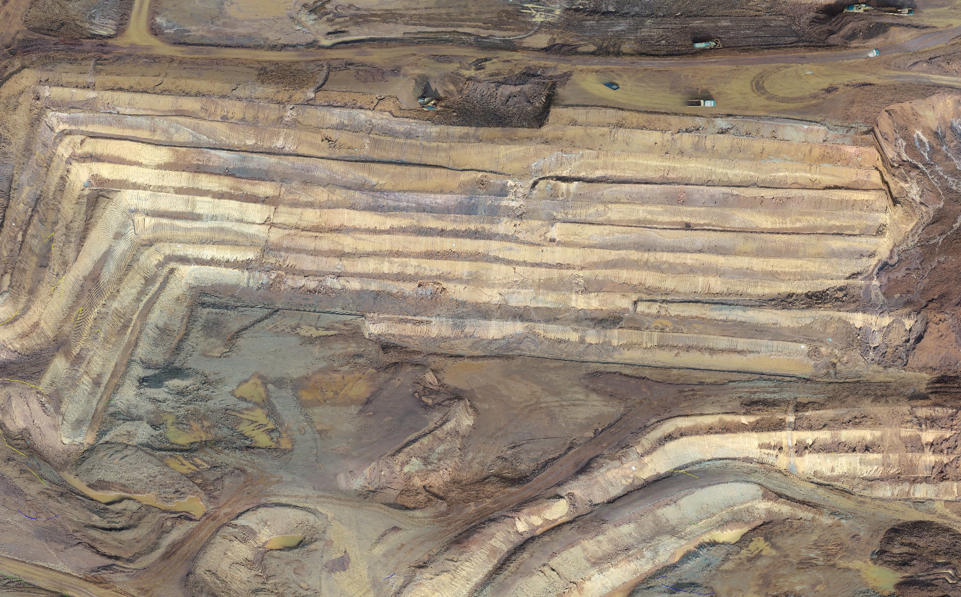 Aerial view of an open-pit mine with terraced excavation levels and exposed earth tones, showing mining activity and access roads.