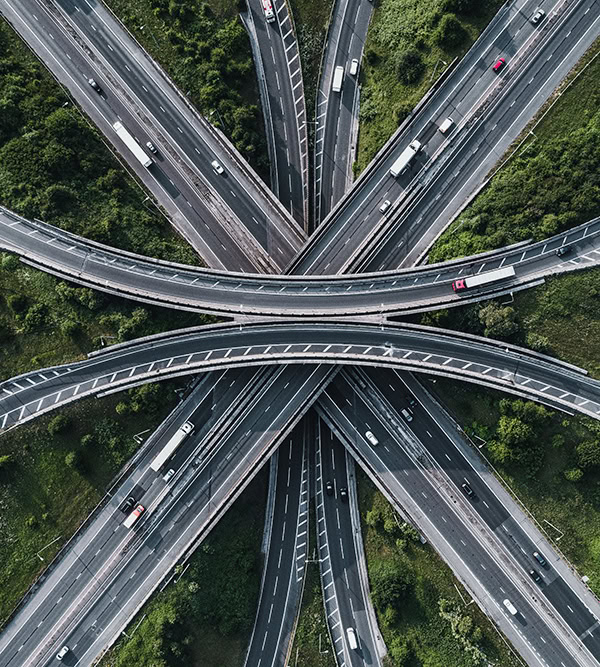 Aerial view of a complex highway interchange with multiple roads intersecting amid green landscape and moving vehicles.