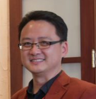 Dr. Liu, a smiling Asian man wearing glasses and a burnt orange blazer, standing indoors.